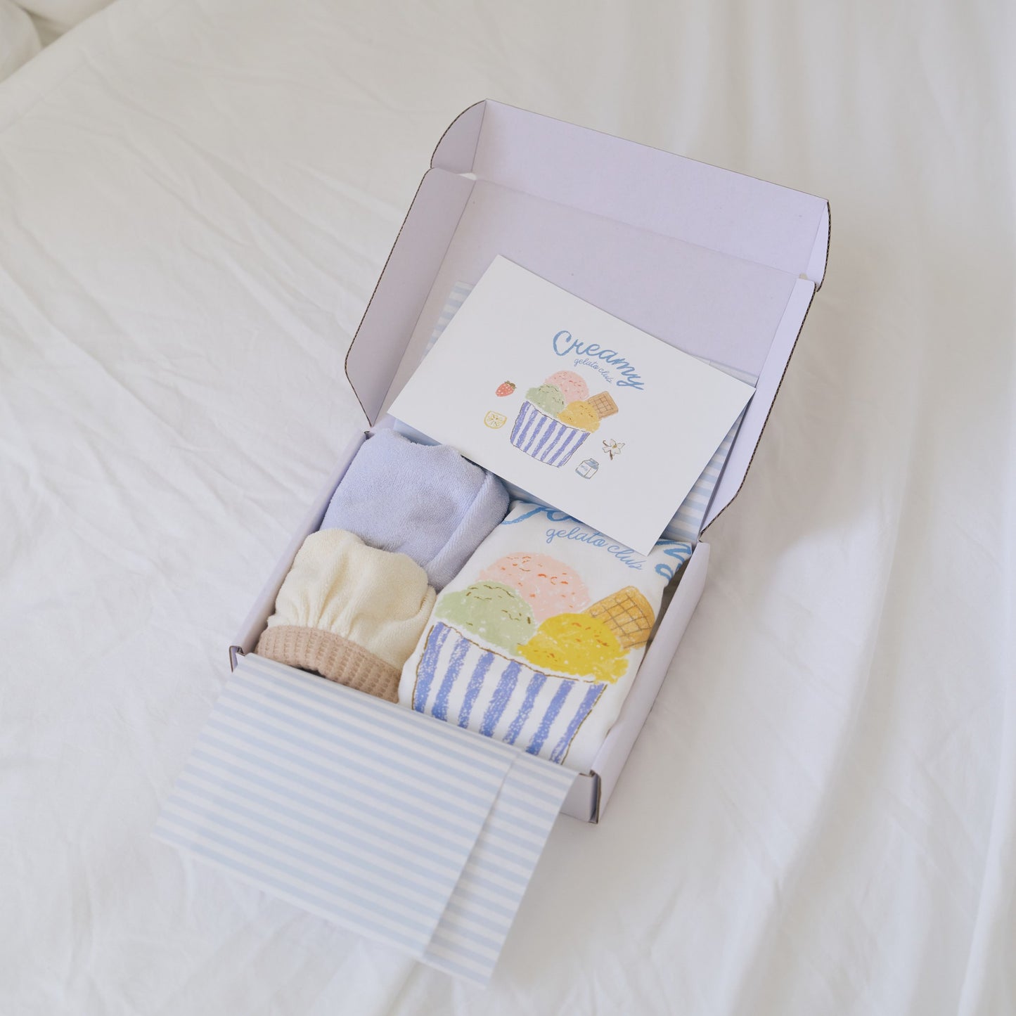 Creamy gift box opened showing romper, bibs, printed card and tissue