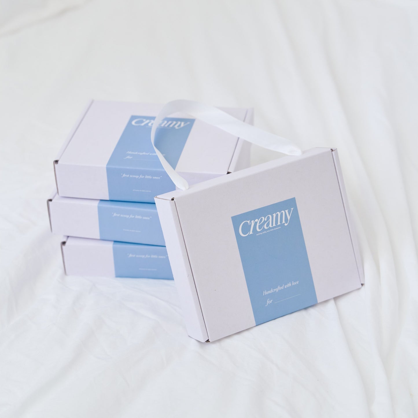 Creamy white gift box with blue band and ribbon handle